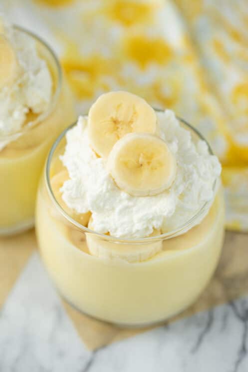 close up of banana pudding in glass serving dish with fresh banana slices and whipped cream