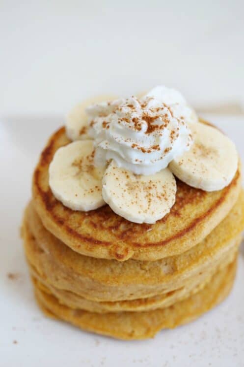 overhead view of a stack of sweet potato pancakes with banana slices and whip cream with cinnamon sprinkled